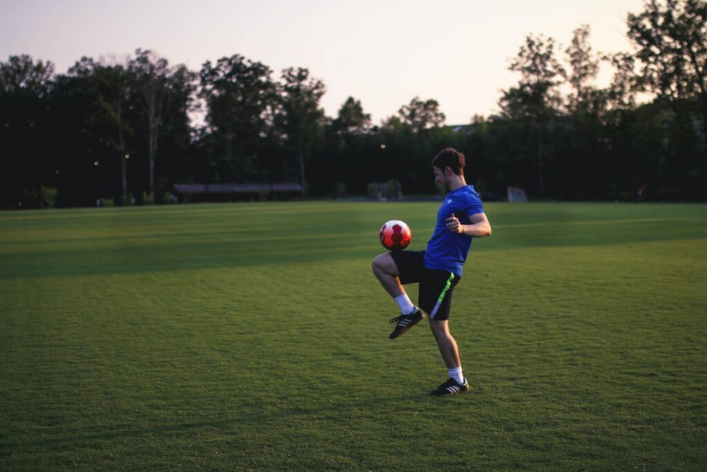 Young man standing alone in a grassy field while balancing a soccer ball on his knee