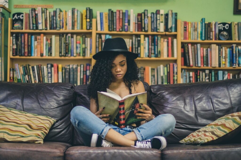 Teen girl wearing a black hat sits on a couch and reads a book