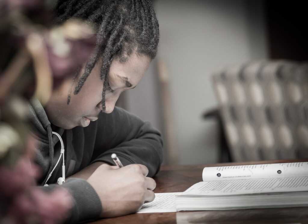 Student looking down at paper he is writing with textbook open in front of him